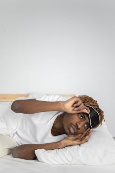Young African American man relaxing in bed with a sleep mask, creating a calm and restful atmosphere.