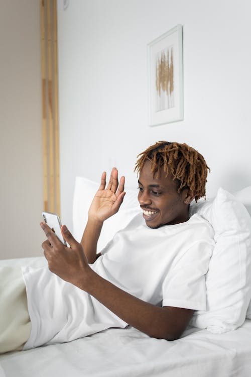Free Man Reclining on His White Bed while Using His Cellphone Stock Photo