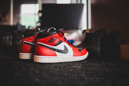 Pair of stylish red sneakers placed on floor with black carpet in room in daytime