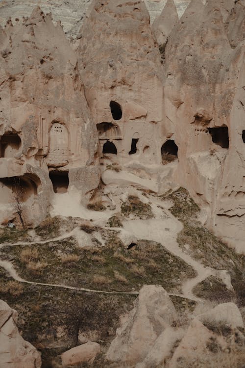 Free Ancient high rocky formations with carved holes located on grassy ground in old famous national park of Cappadocia in Turkey Stock Photo