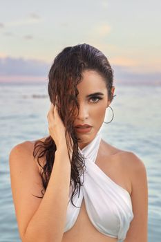 Elegant beach portrait of young woman in a white criss cross top by the sea.
