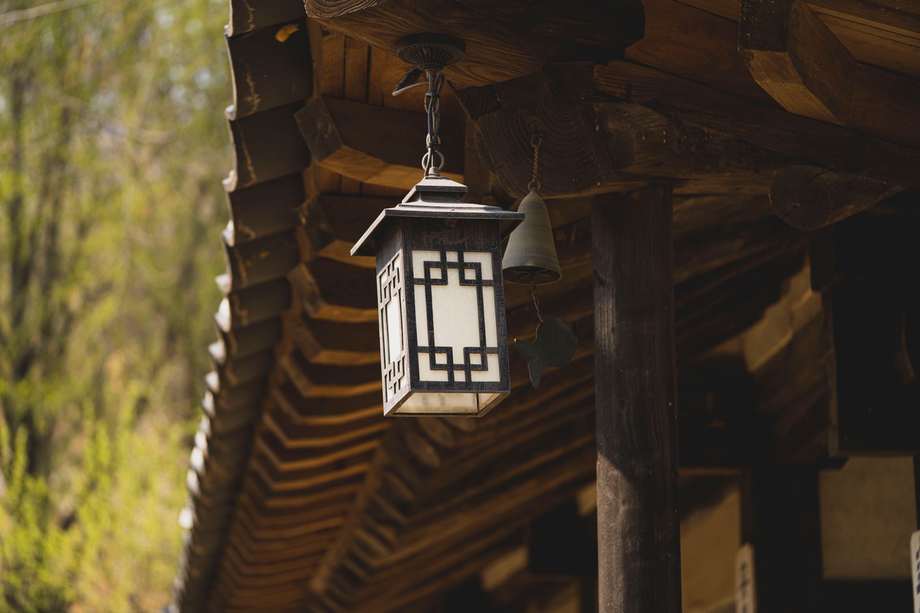 Rustic wooden lantern hanging under the eaves of traditional Korean architecture in sunlight.