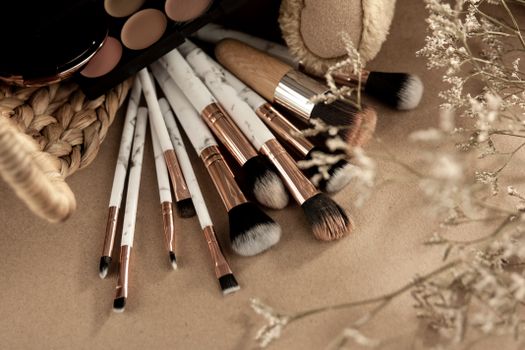 From above of makeup brushes with eyeshadows on beige background with branches of dried plants
