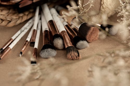 Clean makeup brushes spread out on beige table near wicker basket with eyeshadow and dried grass