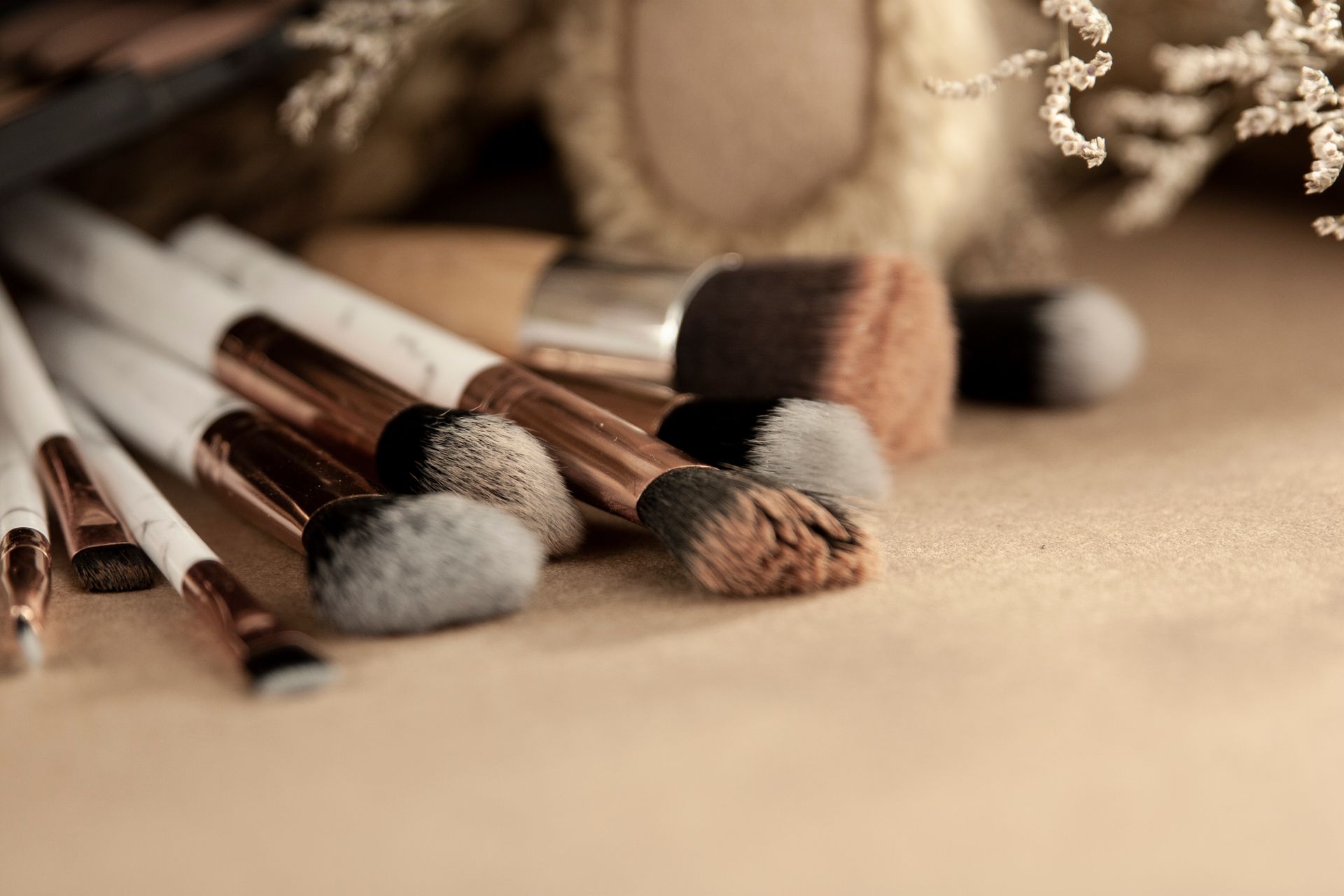 Professional makeup brushes with various types of combs for different beauty products placed on beige table near toy and dried flowers