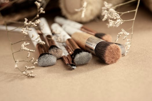 Bunch of professional makeup brushes for different beauty products spread out on beige surface near dried white flowers