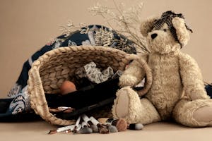 Teddy bear with bow placed near wicker basket with beauty products and set of makeup brushes on beige surface