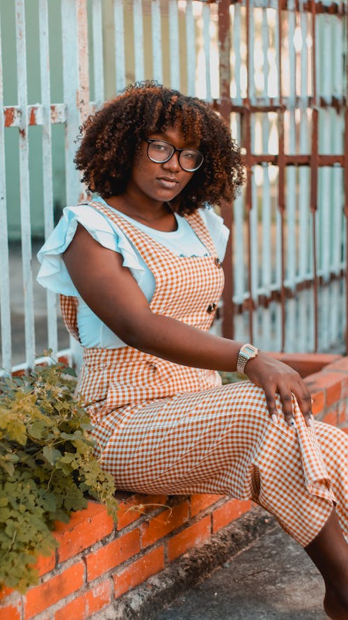 A Woman in Checkered Overalls Sitting on a Plant Box