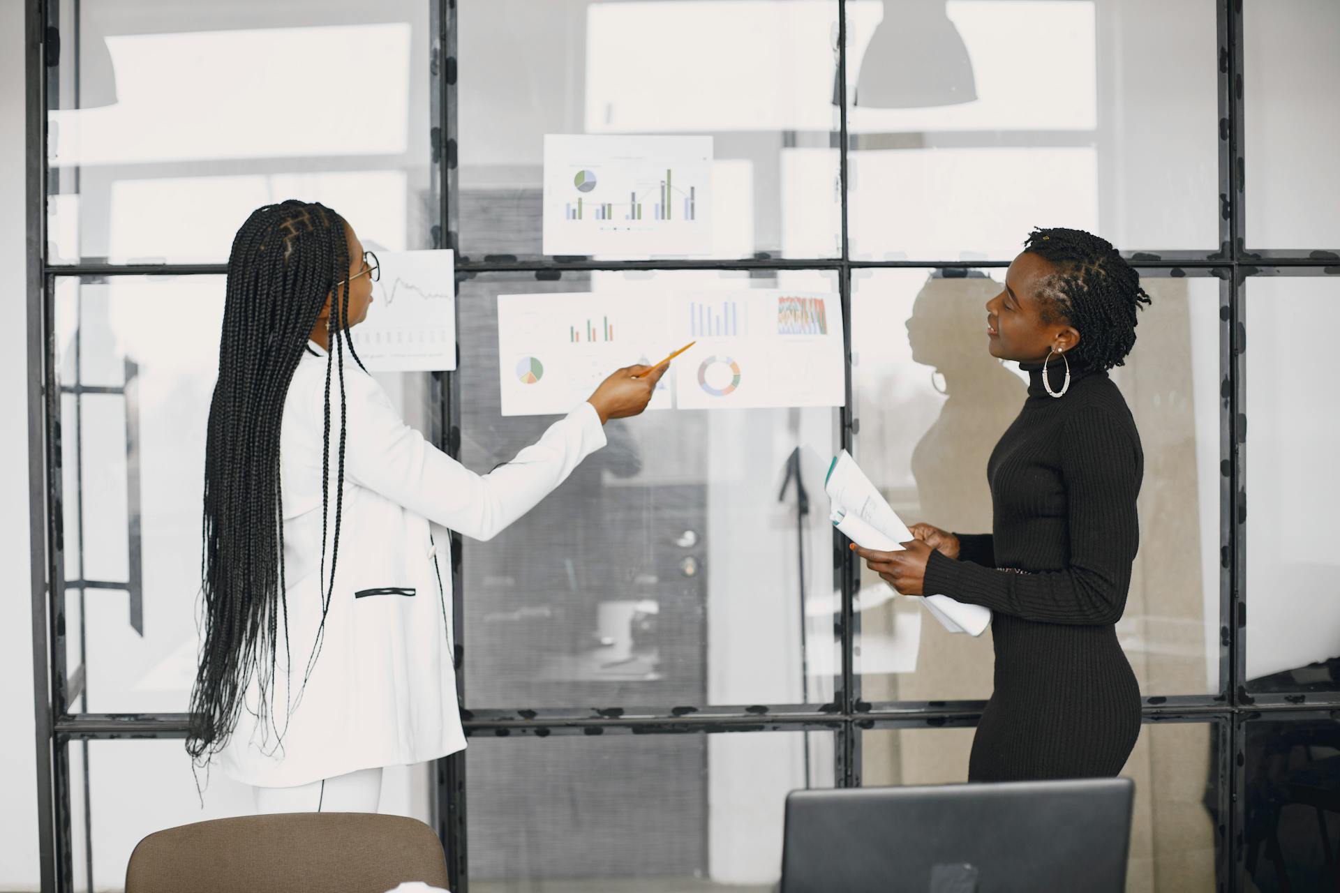 Two businesswomen discussing financial charts in a modern office setting.