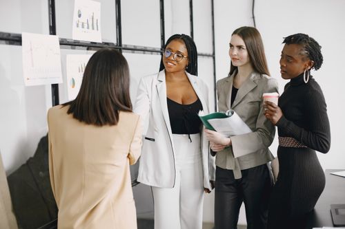 Free Four women having a discussion during an office presentation, displaying teamwork and collaboration. Stock Photo