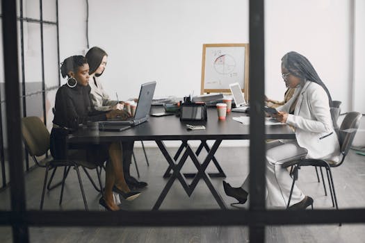 Three women engaged in teamwork and discussion around a table in a modern office setting.