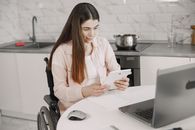 Woman in wheelchair engaged with tablet at kitchen table, creating an inclusive work environment.