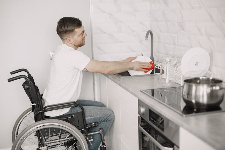 A Man On A Wheelchair Washing A Dish