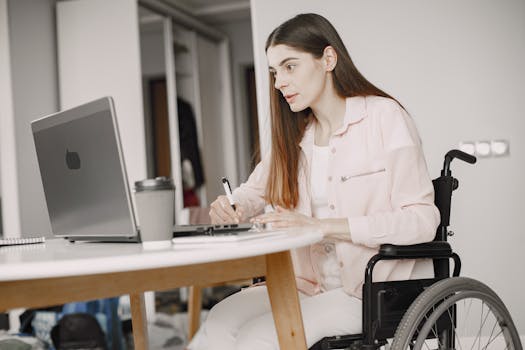 Woman in a wheelchair working remotely at home with a laptop and taking notes, showcasing remote work and accessibility.