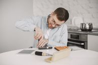 Man wearing glasses using a screwdriver to fix a device on a kitchen table.