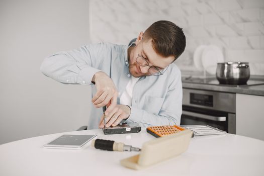 Man wearing glasses using a screwdriver to fix a device on a kitchen table.