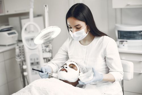 Free A spa professional applying a facial mask to a client in a modern clinic setting. Stock Photo