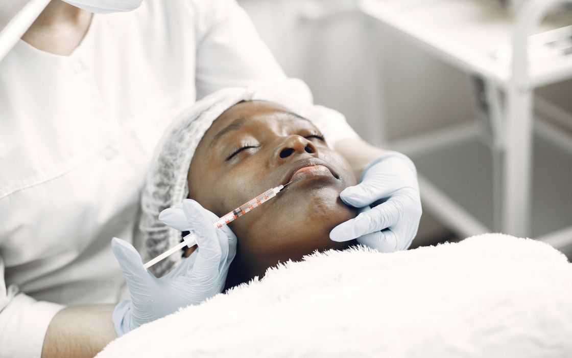 A beautician performs a delicate lip injection on a woman lying with eyes closed.