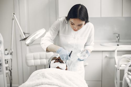 Free Woman provides facial treatment to patient in a spa setting, ensuring relaxation and care. Stock Photo