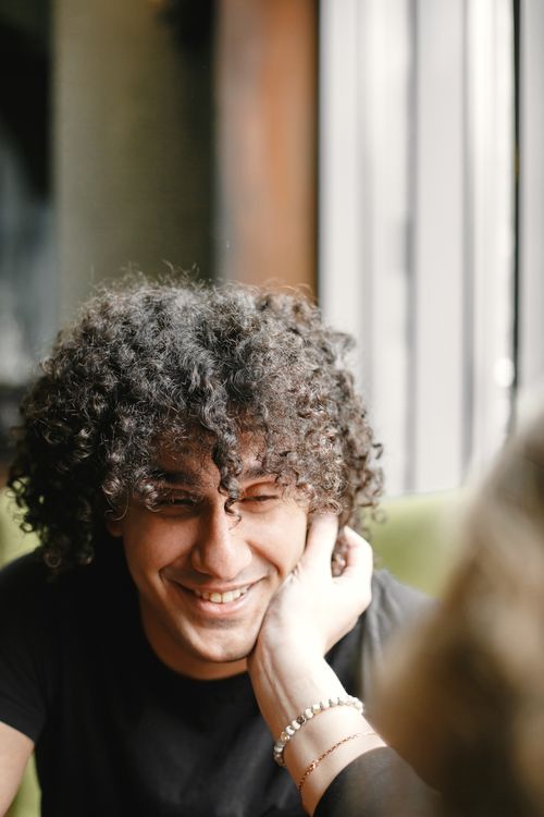 Free Man with curly hair smiling while being caressed in a warm, sunlit room. Stock Photo
