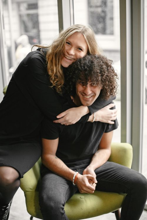 Free A joyful couple embraces and smiles indoors by a large window, radiating warmth and happiness. Stock Photo