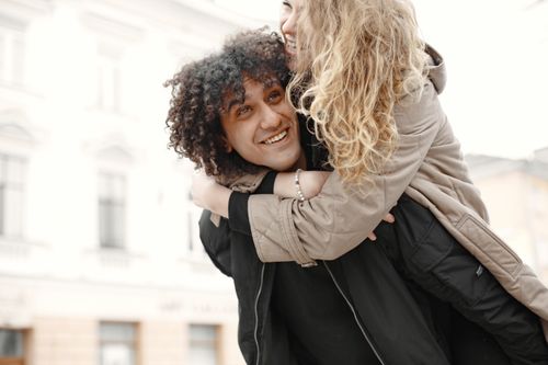 Free Happy couple enjoying a playful piggyback ride in an outdoor setting. Stock Photo