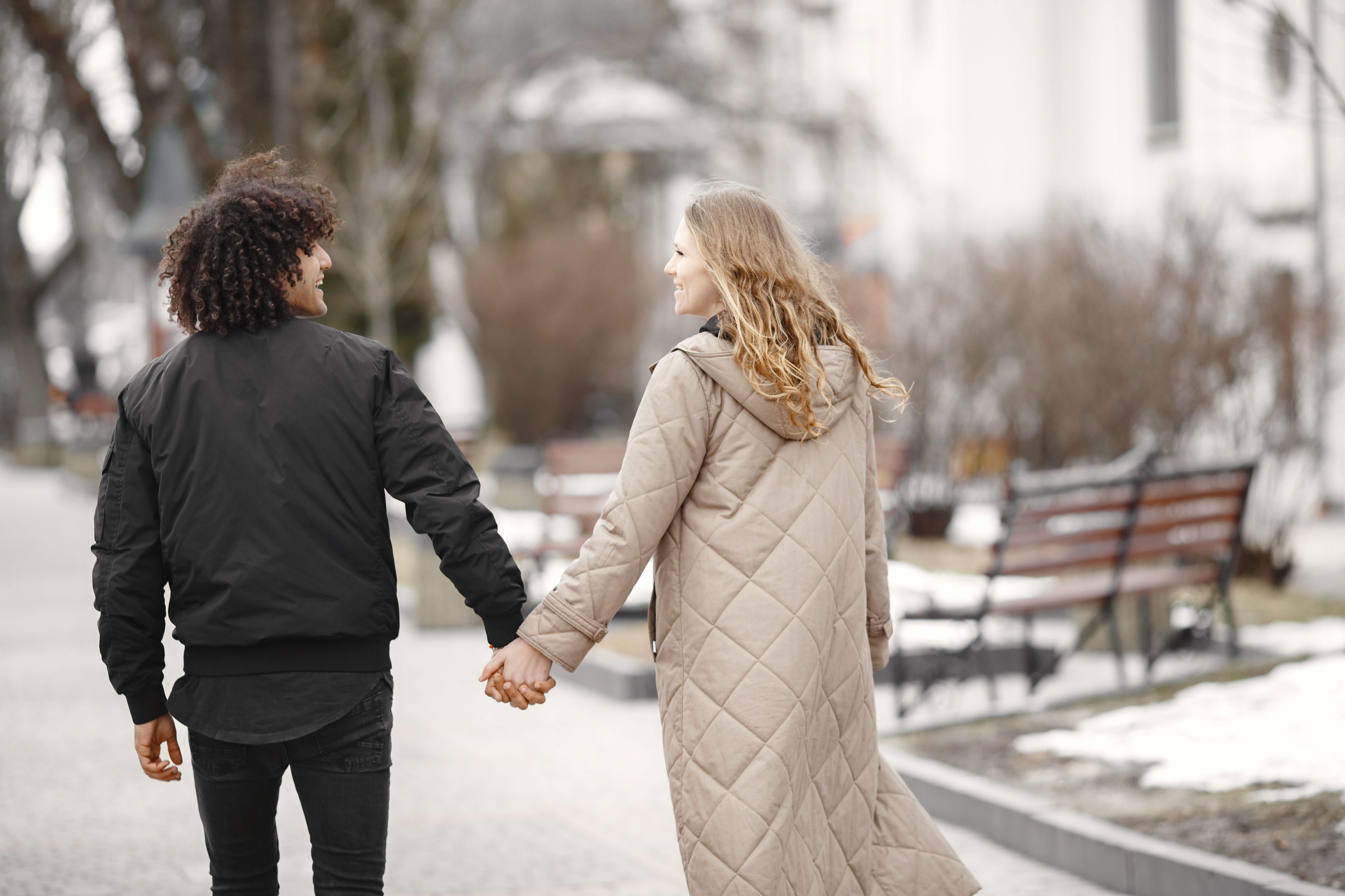 A happy couple walking hand in hand during a winter day, wearing cozy coats outdoors.