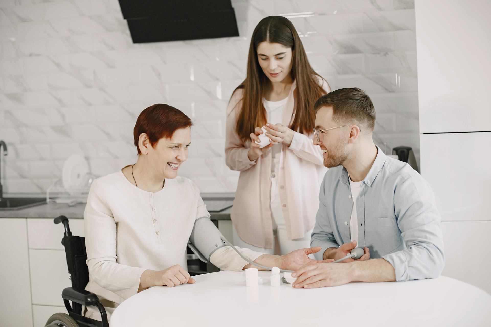 A cozy family moment as an elderly woman has her blood pressure checked by a younger man, with another woman nearby.