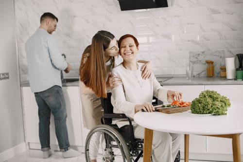 Free A heartwarming scene of family bonding in the kitchen, featuring a woman in a wheelchair being affectionately embraced. Stock Photo