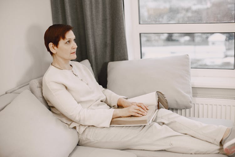 A Mature Woman Sitting On Sofa Reading A Braille Book