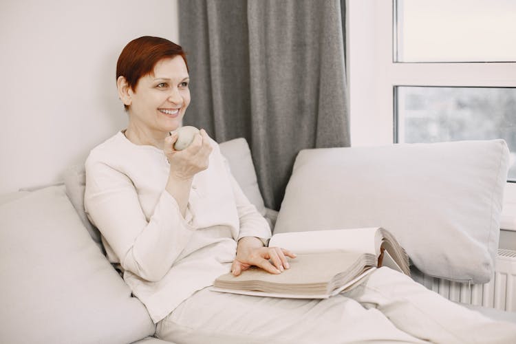 Mature Woman Sitting On A Couch And Reading A Book 