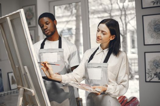 Two artists collaborate in a well-lit studio, focusing on creating art.