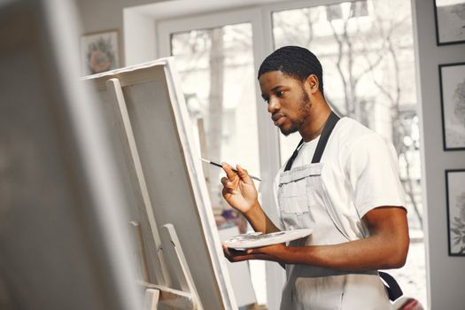 A focused African American artist painting on a canvas indoors.