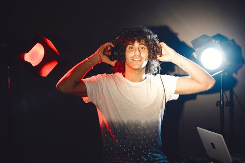 Free Confident male musician in a music studio wearing headphones, surrounded by professional lighting. Stock Photo