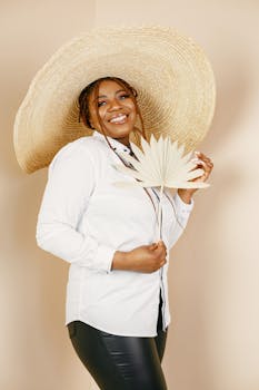 Young woman posing elegantly in a studio with a large straw hat and decorative leaf.