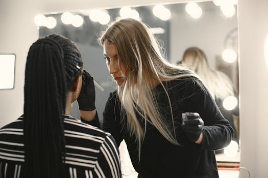 Makeup artist skillfully applies makeup on client in a well-lit studio with mirror lights.