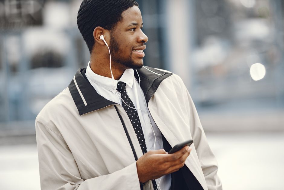 Confident young man with earphones and smartphone in a business suit outdoors.