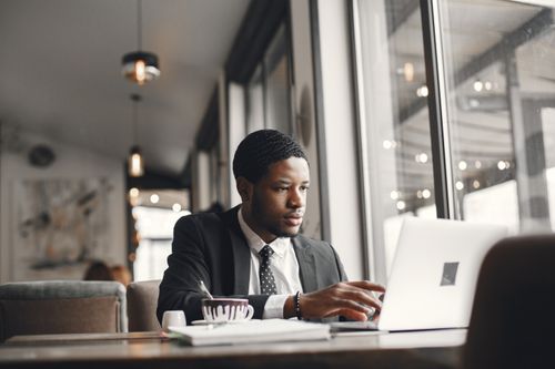 Free Focused businessman working on a laptop in a stylish cafe setting. Stock Photo