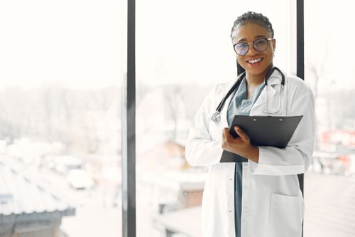 Free Professional female doctor smiling confidently holding a clipboard indoors. Stock Photo