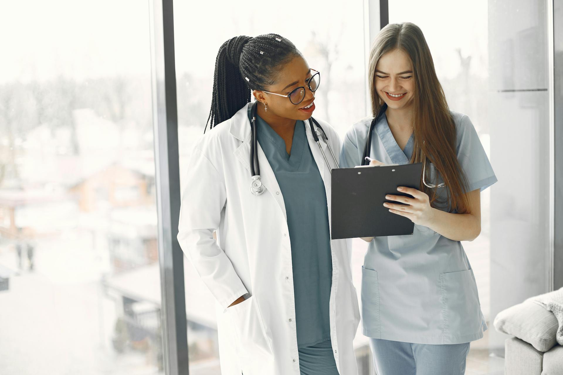 Two female healthcare professionals discussing documents in a bright medical setting.