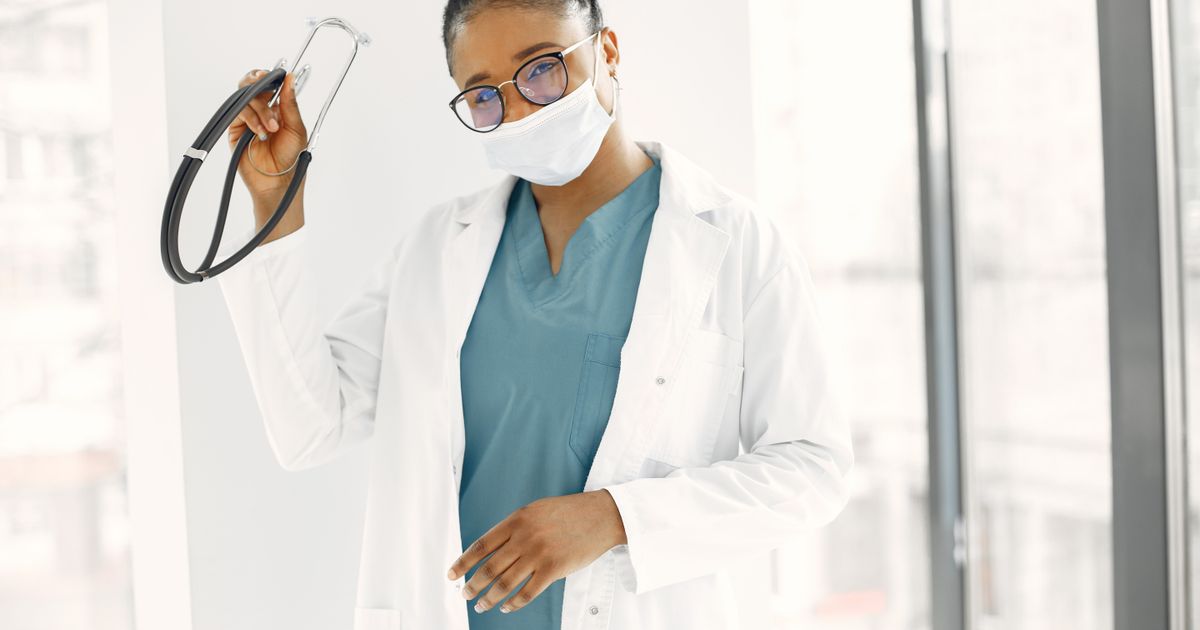 A health worker in a white lab gown holding a stethoscope.