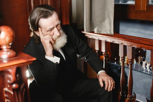 Free A pensive elderly man with a gray beard in a formal suit sitting indoors, captured in natural light. Stock Photo