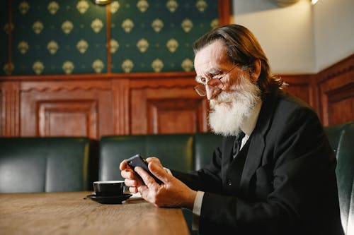 A Bearded Man Wearing Eyeglasses Using His Cellphone while Sitting on a Couch