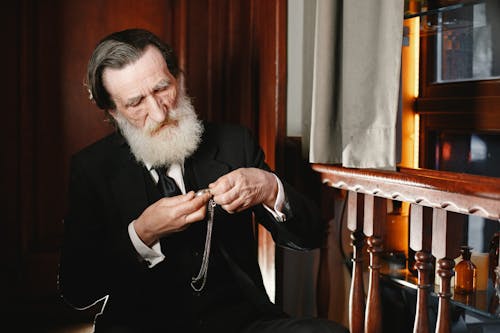 An Elderly Man Sitting on a Chair while Looking at the Pendant Watch he is Holding
