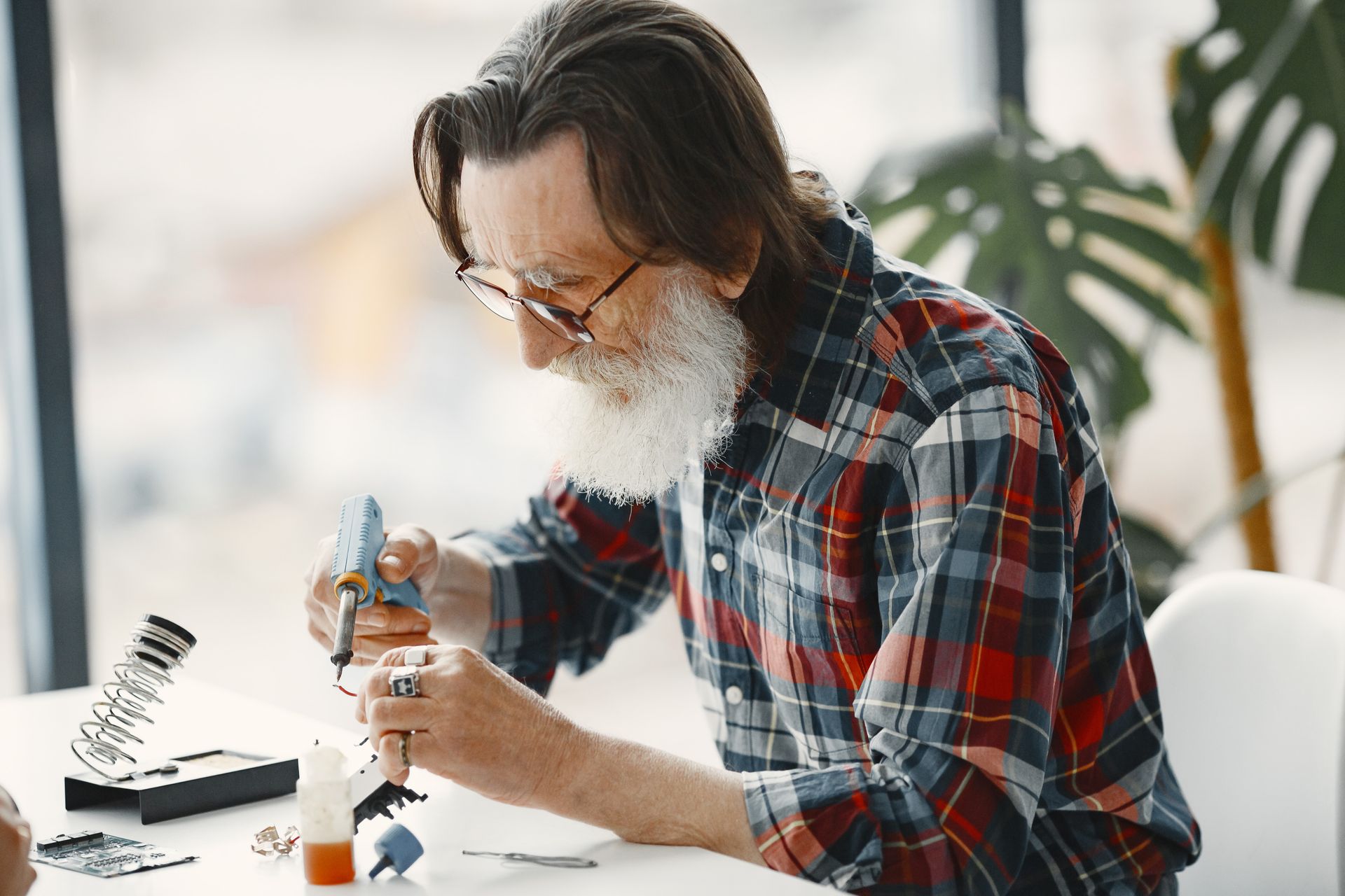 Senior man in checkered shirt concentrating on fixing electronics with tools at hand.