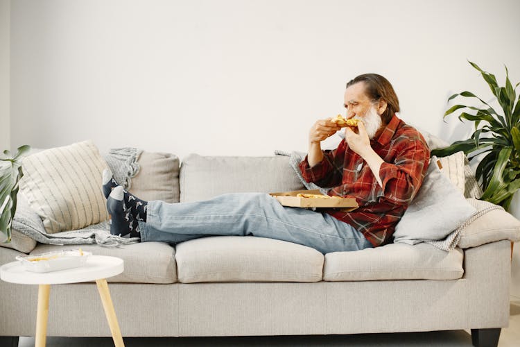 Close-Up Shot Of A Man Eating Pizza While Sitting On A Couch