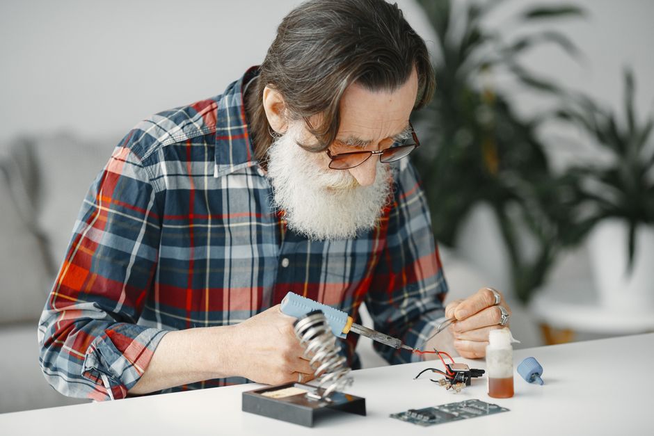Elderly man soldering electronic components, focused on tinkering at home.
