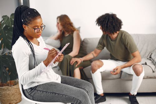 Free Counseling session with a woman taking notes as a couple discusses in the background. Stock Photo