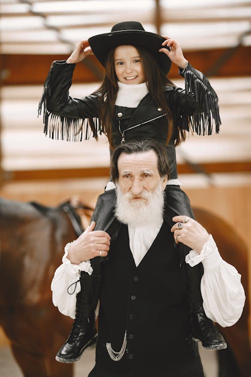 Girl Sitting on Her Grandfathers Shoulders and a Horse in the Background 