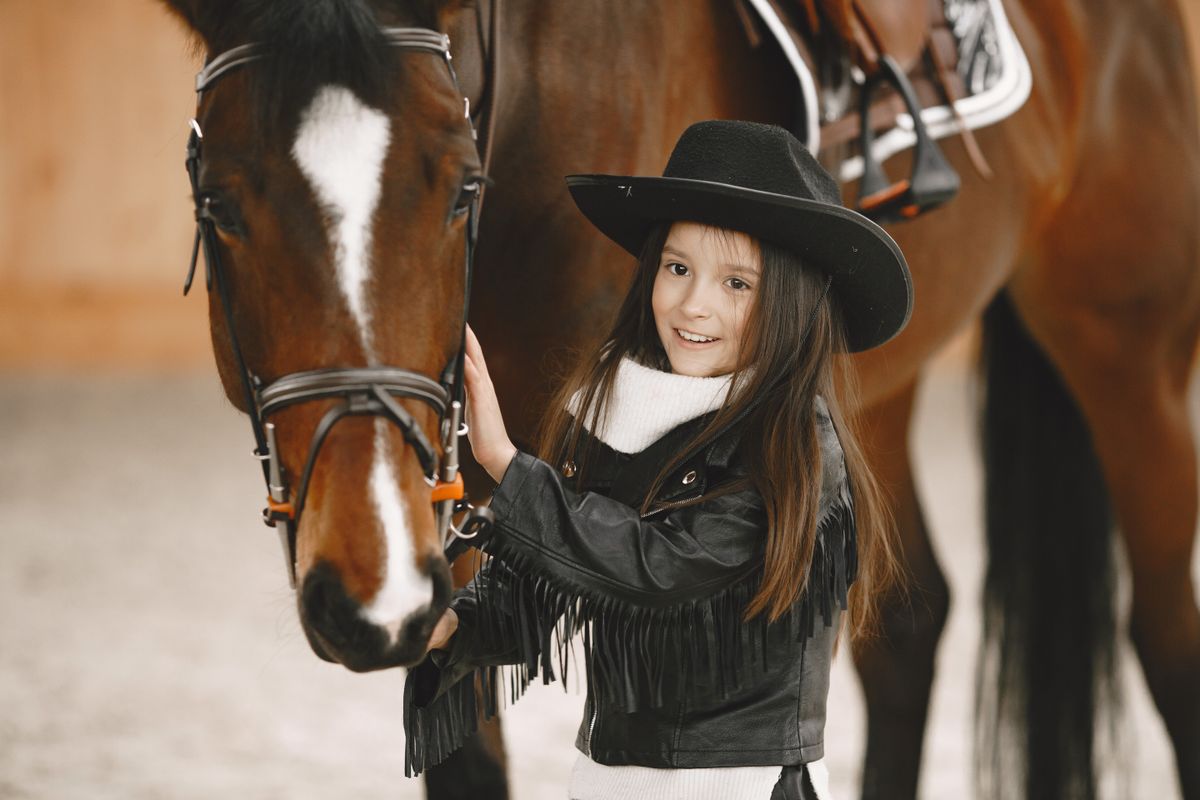 A cheerful young girl in a cowboy hat spending time with a horse